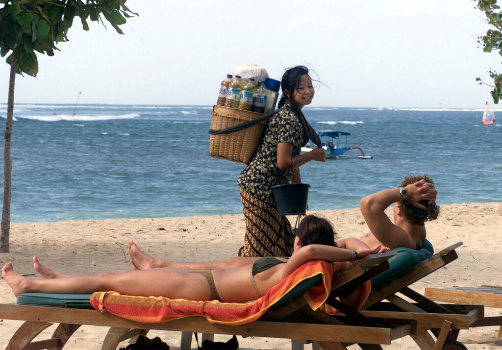 A local fruit vendor passes foreign tourists on Bali in this June 2002 photo. At least 150 people, mostly foreign tourists, were killed in a bomb attack October 12, 2003 in a nightclub on the popular tourist resort island in Indonesia. Australia's flagship airline Qantas has scheduled additional flights to evacuate Australians from Bali following yesterdays explosions. REUTERS/Dadang Tri/FilesReuters